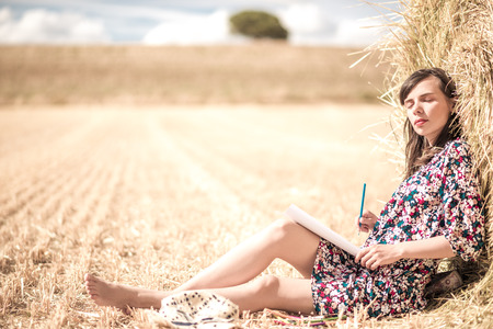 the brunette sitting on the hay and coloring, with different bright pencils and slim legs and hat. closed eyesの写真素材