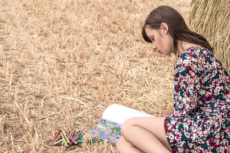 the brunette sitting on the hay and coloring, with different bright pencils and slim legs and hat.の写真素材