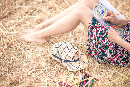 sitting on the hay and coloring, with different bright pencils, colorful dress and slim legs and hatの写真素材