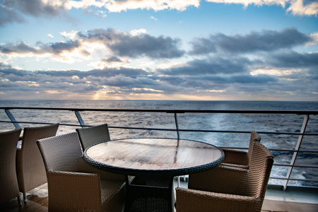 Empty table and chairs in a cafe on the deck of a cruise ship during a sunsetの写真素材