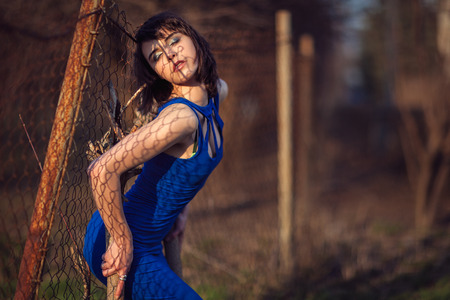 Beautiful girl in evening dress blue backs pressed against the fence の写真素材