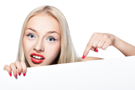 Blonde peeking out from behind a poster on which you can make advertising inscription or image の写真素材