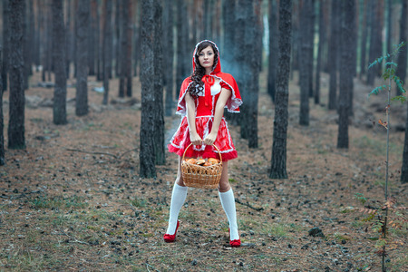 Beautiful girl in a red raincoat alone in the woods with a basket in which cakes の写真素材