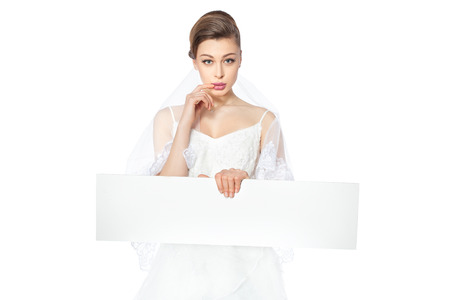 Beautiful bride hesitate showing blank poster on which to make an inscription の写真素材