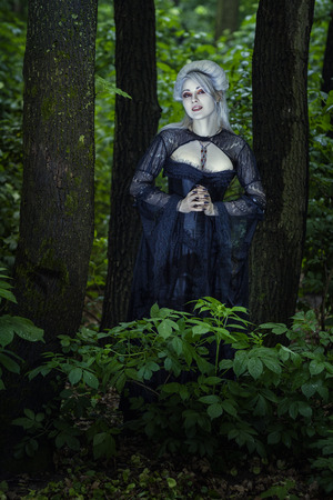 Beautiful girl witch in black dress stands alone in the woods の写真素材
