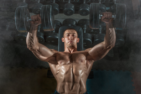 Bodybuilder man lying exercisers squeezing large dumbbells の写真素材