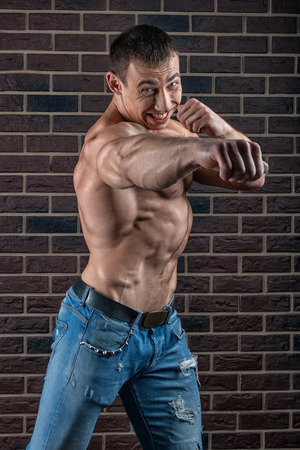 Man with big muscles punches ahead brick wall background の写真素材