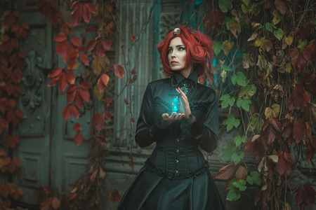 Fabulous girl with red hair, she is holding an hourglass. At the door of the castle.の写真素材