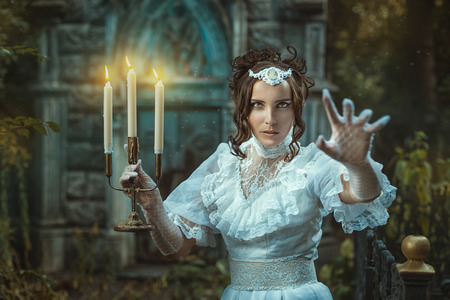The evening darkens. Girl with a candelabra in hand in which candles are burning. Girl scares us and shouts inducing intense fear.の写真素材