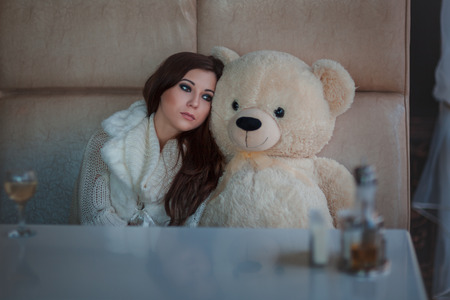 Sad girl with toy bear sitting at the table.の写真素材
