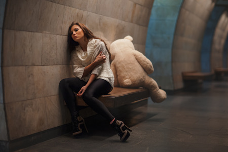 Girl sitting on a bench facing away from the toy bear, they quarreled and sadness.の写真素材