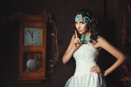 Girl stands near the old clock and puts his finger to his lips.の写真素材