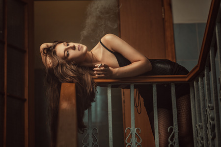 Woman blowing smoke lying on the railing at an stairwell.の写真素材