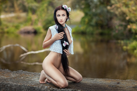 Beautiful naked girl with long hair sitting near the lake.の写真素材