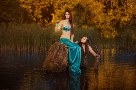 Fairytale sad woman sitting on a stump in the marshes, in the back looks fabulous man.の写真素材