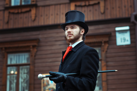 Man in a retro style with a cane in the cylinder is on the street.の写真素材