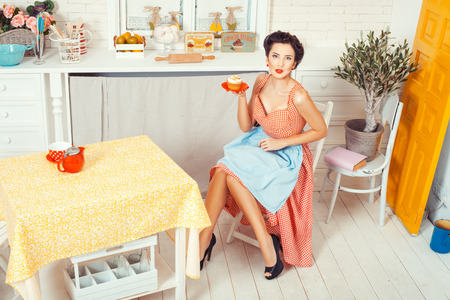 Pin-up girl style. The view from the top. Girl sitting on the middle of the kitchen and holding a saucer muffin.の写真素材