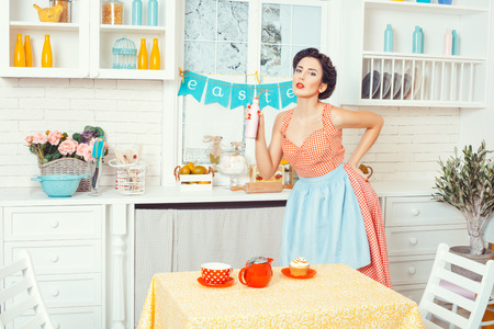 Pin-up girl style. Girl standing in the kitchen and holding a bottle of drink.の写真素材