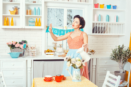 Pin-up style. Woman in an apron in the kitchen stands and watering flowers. Look at her nails on the arm.の写真素材
