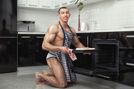 Bodybuilder man in apron preparing in the kitchen.の写真素材
