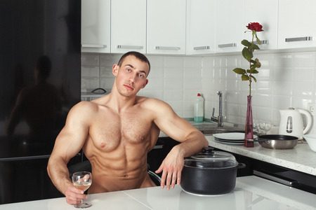 Naked man resting in the kitchen with his hand on the pan.の写真素材