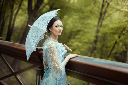 Portrait of a girl in the forest her oldfashioned dress. In her hands she holds a vintage umbrella.の写真素材