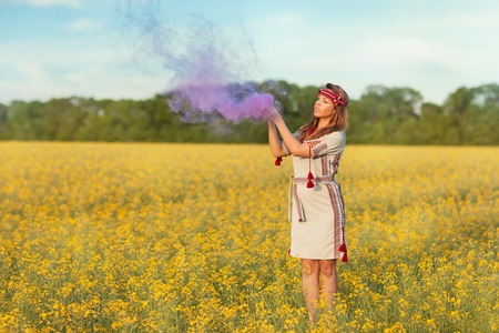 A girl stands in a field of yellow flowers she raised her hands to the sky and released purple smoke.の写真素材