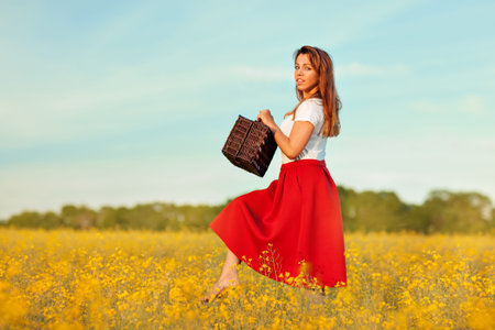 A girl walks on a meadow. Meadow of yellow flowers in bloom. On her white Tshirt and red skirt.の写真素材