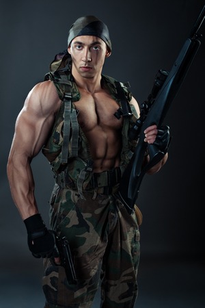 Man with large muscles in military uniform with weapon.の写真素材