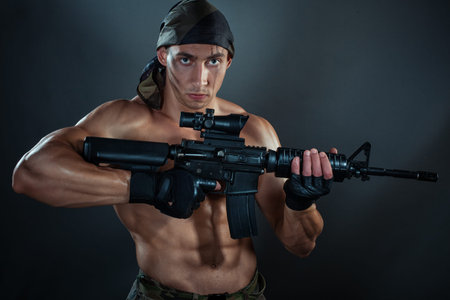 Military man. He is holding an automatic weapon. He has big muscles.