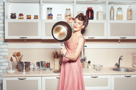 Girl is in the kitchen. She straightens her hair. She looks in the pan like a lady in the mirror.の写真素材