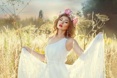The beautiful gentle girl in white dress. She stands in a field in the grass.の写真素材