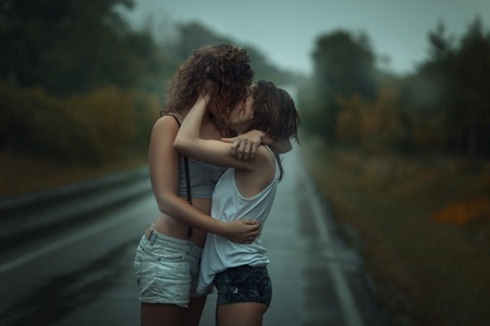 Girls standing in the rain on the street. They hug each other.の写真素材