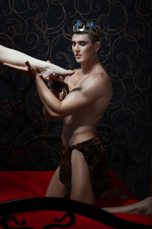 King holds a female leg in hand. On his head crown.の写真素材