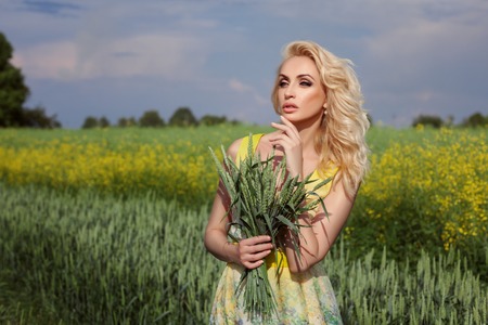 Girl stands in a field. In the background, yellow flowers. She's blonde.の写真素材