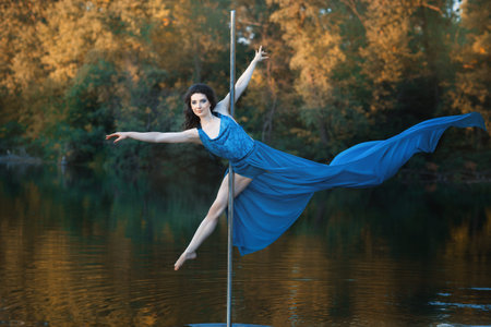 Girl in a flowing dress is dancing around a pole dance. Outdoors on the river.
