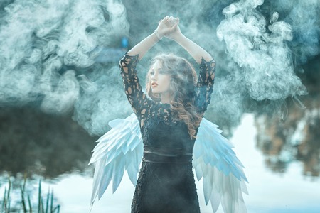 Girl with angel wings is shrouded in smoke. This occurs in the open air on a river.の写真素材