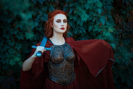 Red-haired girl warrior. In hands holds a sword on the chest wearing cuirass.の写真素材
