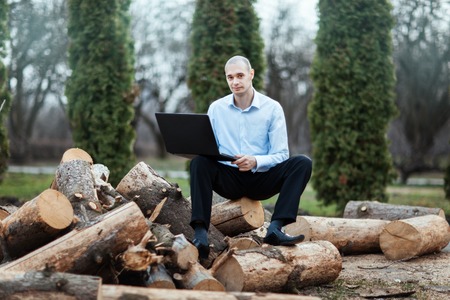 Man sitting on a log and working on a laptop. In appearance he was an intelligent and clever.の写真素材