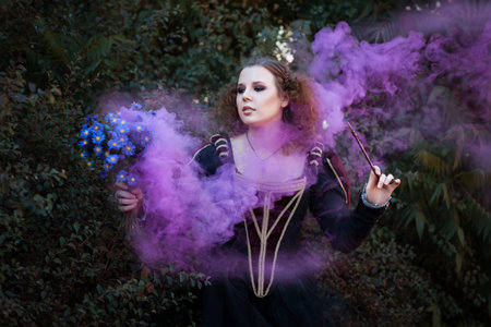 Woman showing tricks with a magic wand. She bewitched a bouquet of flowers from which it is purple smoke.の写真素材