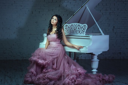 In a dark room girl sitting at a white grand piano.の写真素材
