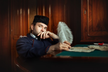 Man with the sad eyes writes a letter. In his hand he holds a quill pen on the desk of the manuscript.の写真素材