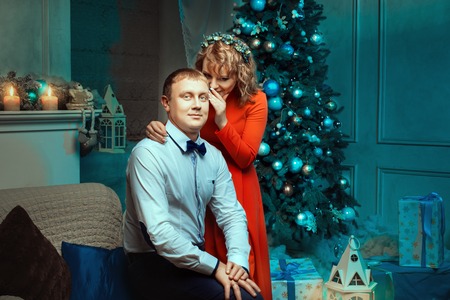 Woman whispering in the ear of a man gentle words New Year's Eve near the Christmas tree ornaments.の写真素材