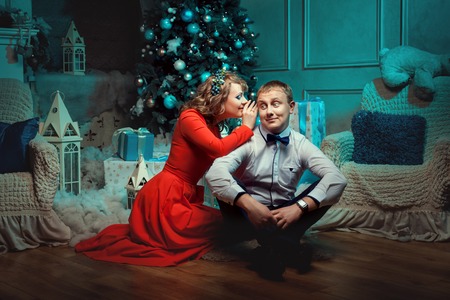 Woman whispering in the ear of the man. They married young couple. Gifts under the Christmas tree.の写真素材