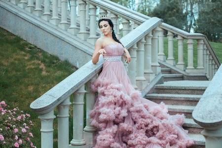 The young queen in a lush pink ball gown standing on the stairs of the castle.の写真素材