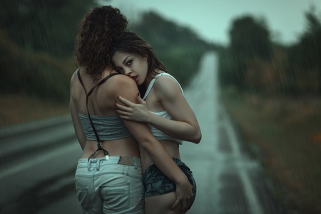 Young women couple have hugs on the road in the rainの写真素材