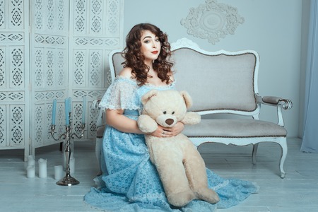 Plump woman with a toy bear sitting on the floor in the room.の写真素材