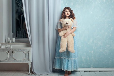 Plump woman hugging toy bear, she stands near a wall like a little girl.の写真素材