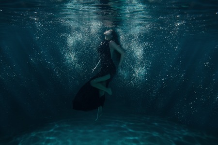 Girl on the ocean floor among the light beams passing through water.