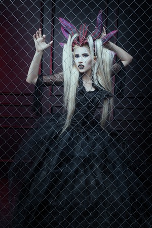 Woman in gothic dress and horns on his head is in the cage.の写真素材